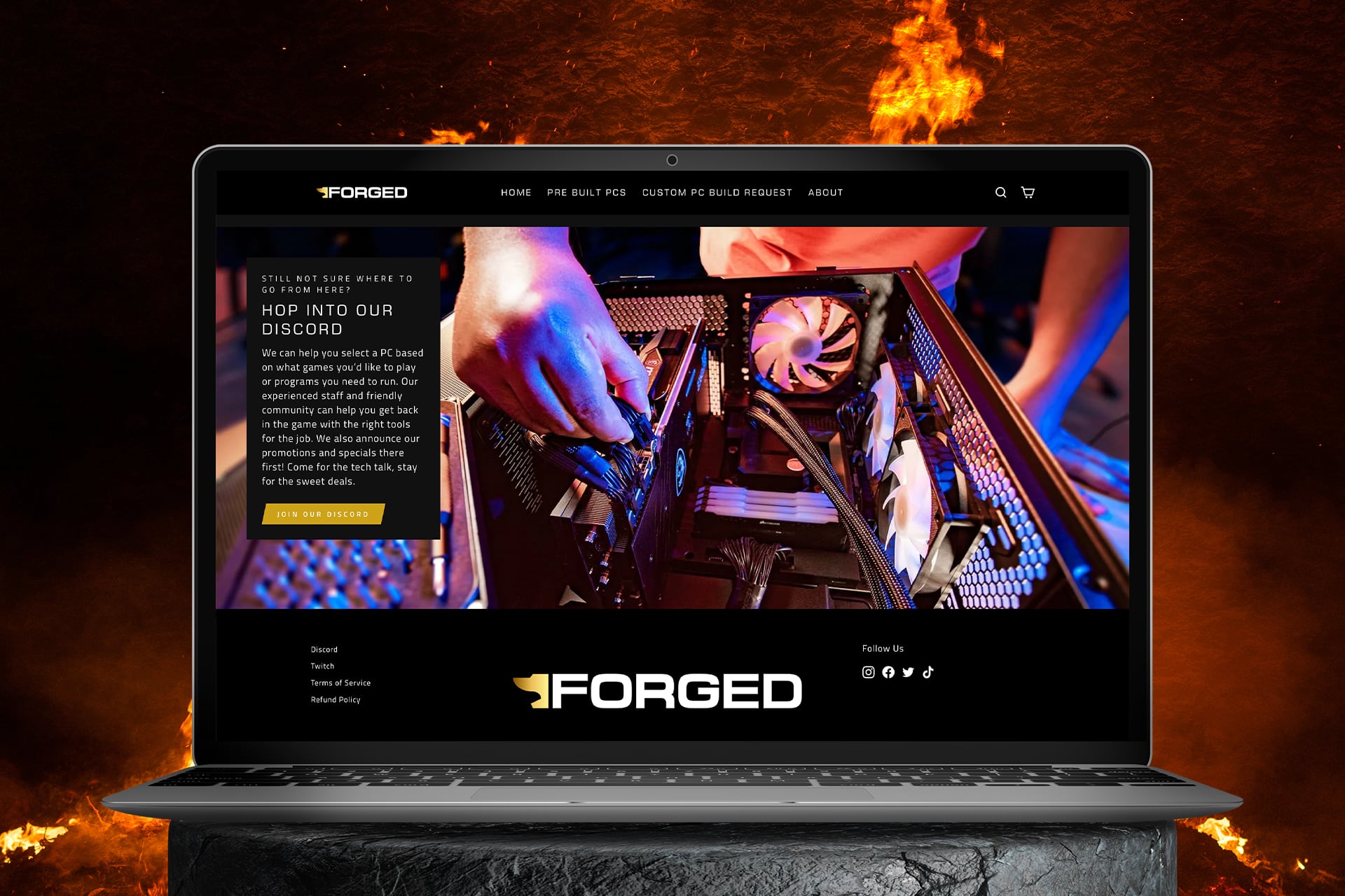 The Forged PCs website displayed on a laptop resting on a stone surface, with flames rising behind it.