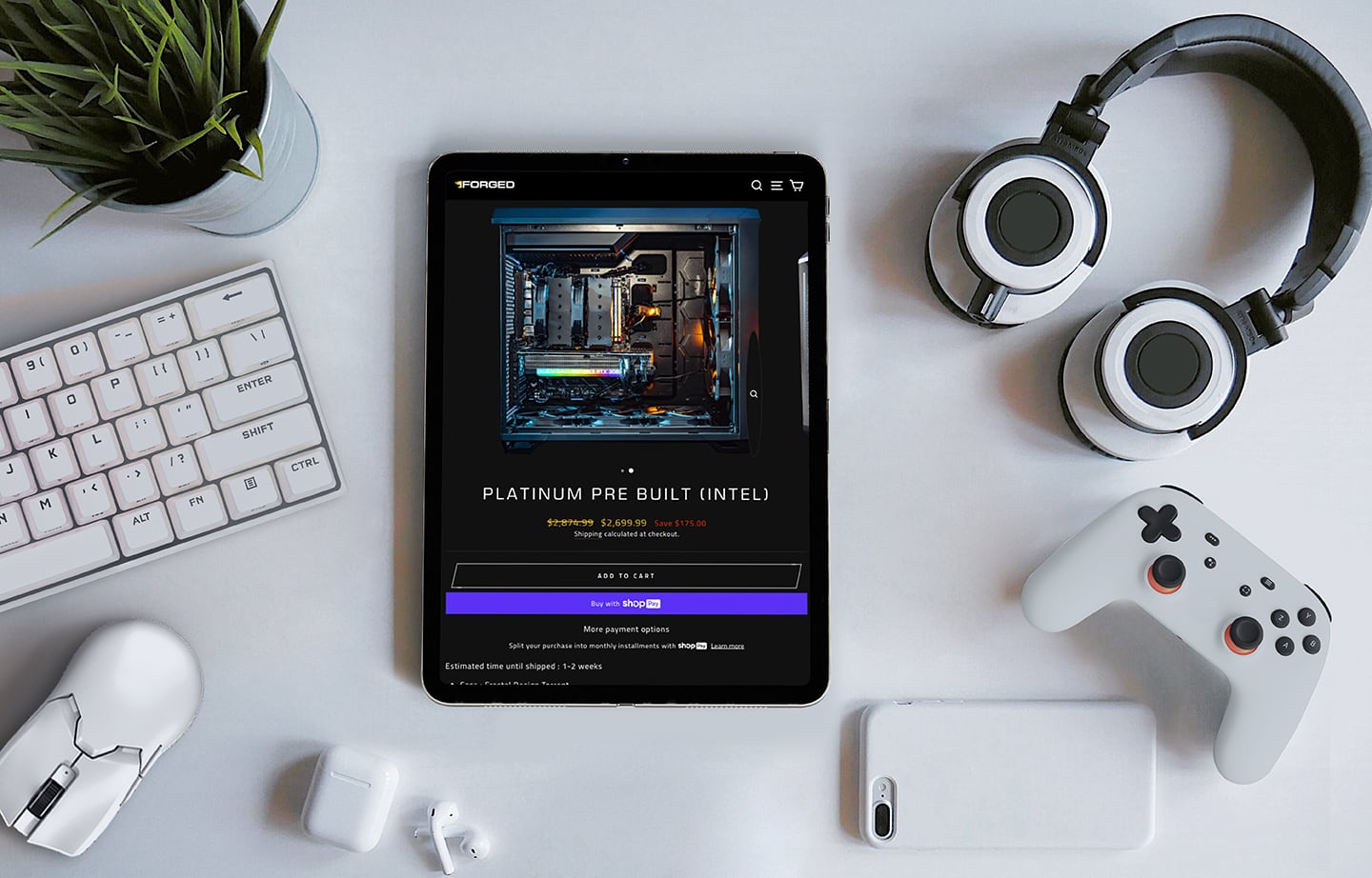 A product page of the Forged PCs website displayed on a tablet, surrounded by gaming and tech peripherals.
