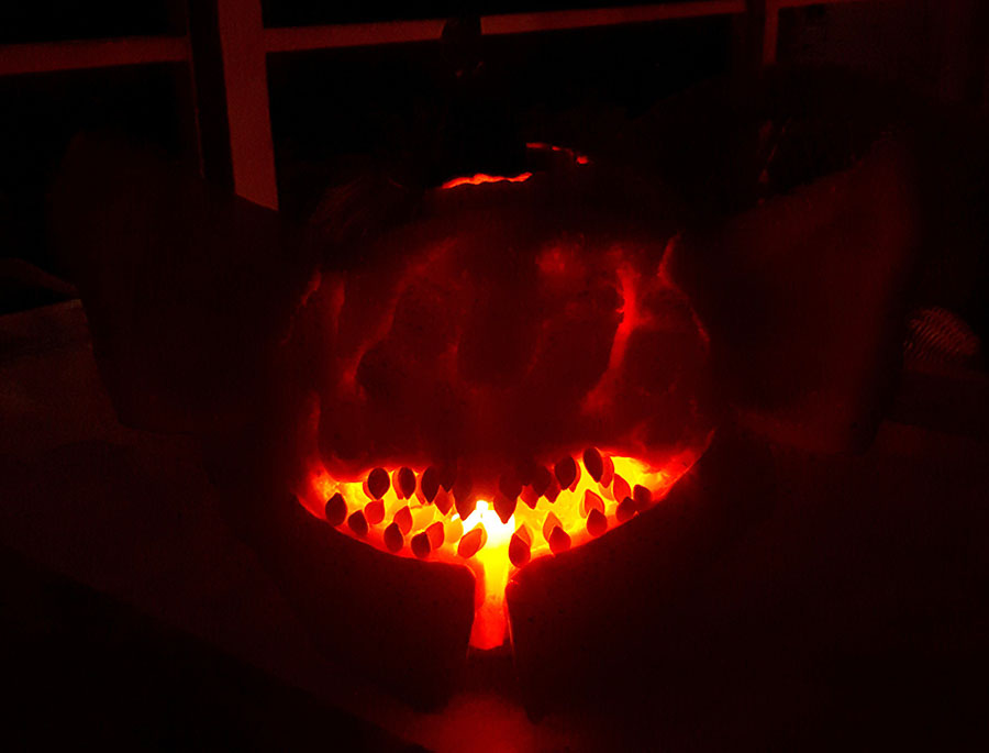 The Riven of a Thousand Voices pumpkin carving at night, with only her toothy mouth glowing from the fire within.