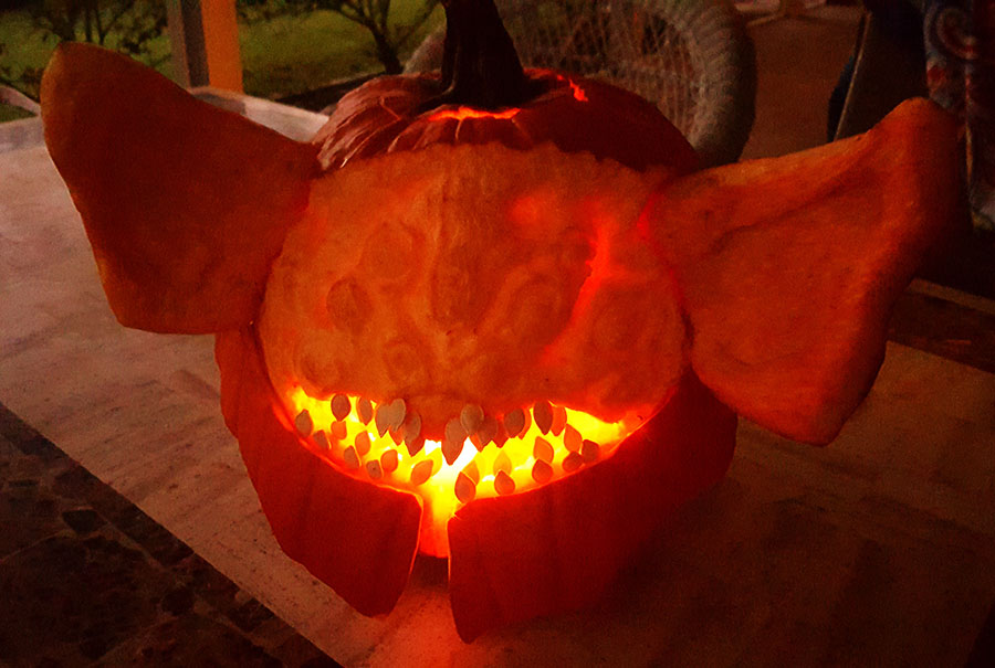 Photo of the Riven of a Thousand Voices pumpkin carving at twilight, with her toothy mouth glowing from within by the jack-o'-lantern candle.